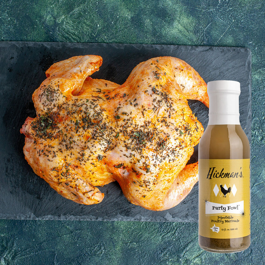 Roasted chicken on a slate board with a bottle of Hickman's Party Fowl seasoning.
